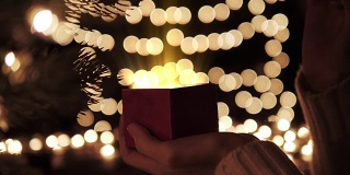 女人打开红色的圣诞礼盒，里面有金色的魔法灯