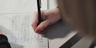 一个女学生在一本练习册上写字。她正在做家庭作业