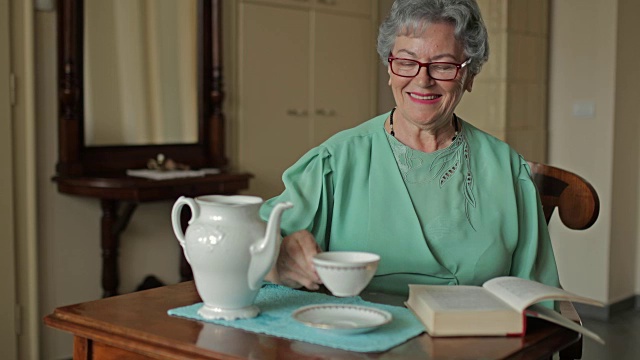 老女人在家里享受着下午茶，看着镜头。