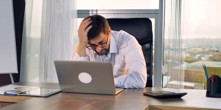 一个悲伤的商人盯着他的笔记本电脑屏幕。