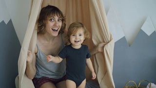 快乐的妈妈和年幼可爱的女儿玩和躲在家里的窗帘后面视频素材模板下载