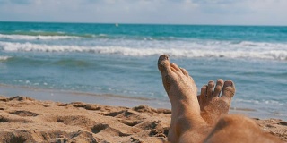 男人的腿躺在海边的沙滩上，POV。慢动作