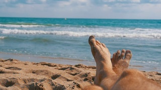 男人的腿躺在海边的沙滩上，POV。慢动作视频素材模板下载