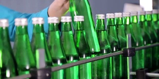 生产线上的一名员工擦拭绿色的矿泉水玻璃瓶。近距离