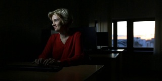 在校园图书馆里，一个学生女孩独自在电脑上完成截止日期的项目，直到晚上，滑动相机日落的背景。金发女郎微笑着