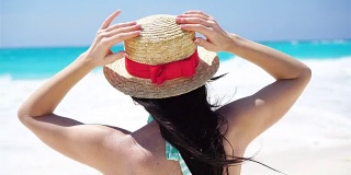 戴着帽子的年轻女子在热带海滩上看着美丽的大海