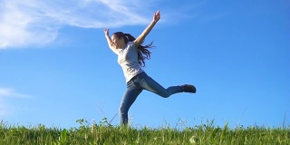 快乐的女孩奔跑在绿色的草山上，对着蓝天