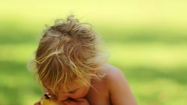 可爱的婴儿宝宝咬了一口梨果。4k剪辑分辨率肖像的金发婴儿吃在户外的阳光