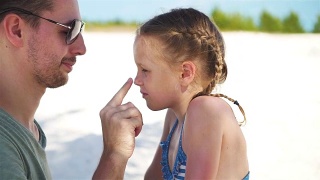 父母在孩子鼻子上涂防晒霜。可爱的女孩在防晒霜的肖像视频素材模板下载
