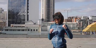 年轻的运动女性玩家戴着增强现实眼镜打拳击玩动作模拟游戏手机app，女性玩家在VR头盔中用拳头格斗，户外虚拟训练新技术
