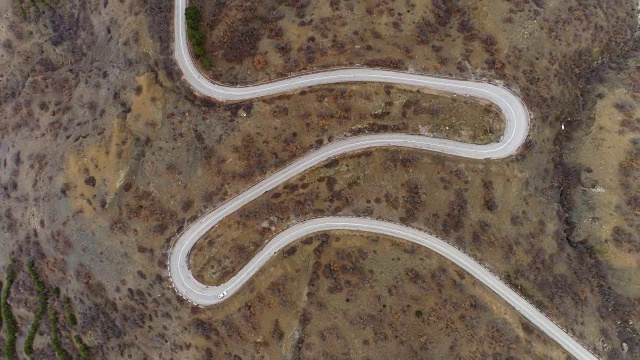 白色汽车在蜿蜒的道路上行驶。绿色的山。鸟瞰图。向上飞。