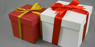 灰色背景下的两个礼品盒。白色礼盒与红色丝带蝴蝶结和红色礼盒与金黄色蝴蝶结支架。