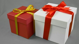灰色背景下的两个礼品盒。白色礼盒与红色丝带蝴蝶结和红色礼盒与金黄色蝴蝶结支架。视频素材模板下载