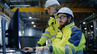 男工业工程师在电脑上工作，女经理在谈项目。他们在重工业制造工厂工作。视频素材模板下载