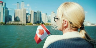 一位举着加拿大国旗的妇女从船上看着多伦多的城市景观。加拿大旅游概念