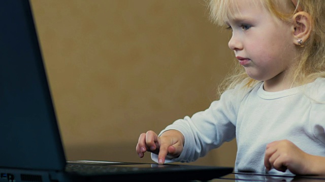 特写:一个三岁的小女孩独立地把卡通片放在笔记本电脑上，在家里的屏幕上看。