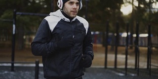 迷人的男人戴着耳机在冬季公园听着音乐为慢跑做热身运动