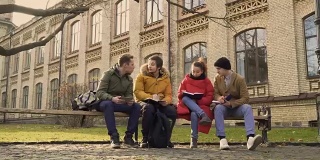 四个学生坐在公园的长椅上