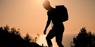 一个背着背包的男人在日落时分爬上了山顶。日落时那个人的剪影。健康积极的生活方式