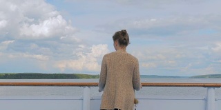 年轻女子站在游轮的甲板上，看着河流和风景