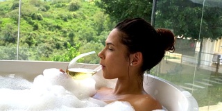 美丽的女人享受着一杯红酒和浴缸里的美景