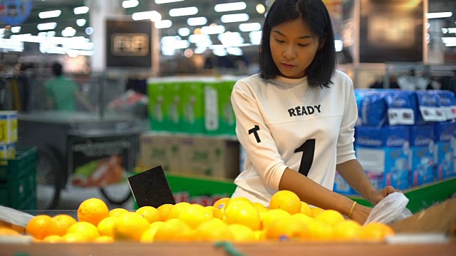 年轻的亚洲女人在杂货店挑选橙子