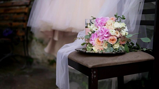 美丽的新娘花束在桌子上与美丽的婚纱和新娘饰品的背景。婚礼礼服在肩膀上，仪式前。美丽的婚礼花束和新娘的礼服