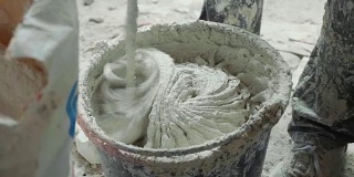 建筑工用电动搅拌机在桶中搅拌白色石膏。