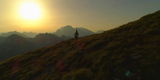 航拍:日落时分，年轻女子爬上山顶的剪影。
