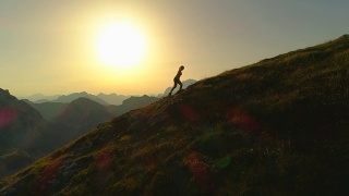 空中剪影:日落时分，一个年轻女子爬上一座山的剪影。视频素材模板下载