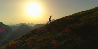 空中剪影:日落时分，一个年轻女子爬上一座山的剪影。