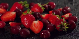在潮湿的黑色表面涂上草莓和樱桃。