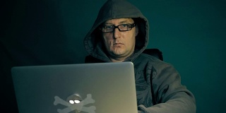 成年白人黑客拿着笔记本电脑坐在桌前。时尚眼镜黑客在互联网上编写开发程序。安全系统。跟踪运动摄像机。