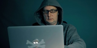 成年人在电脑上浏览互联网。一个人深夜坐在桌子旁，拿着笔记本电脑。他的时尚眼镜屏幕上的闪光。电脑屏幕反映在一个年轻人的眼镜上。缓慢的运动。