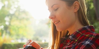 微笑的女人享受自然。坐在绿色公园的长椅上，用智能手表听写信息