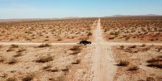 一辆黑色的汽车在沙漠的空旷道路上行驶。