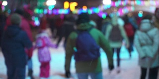 冬季运动概念。晚上在城市溜冰场的人群。一大群开心的人在滑冰。雪下降。圣诞天模糊。运动和好心情的概念。家庭和幸福的夫妇滑冰
