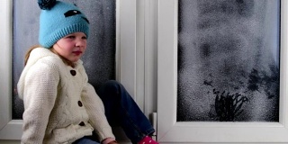 小女孩坐在结冰的窗户后面的窗台上。低的自由度。