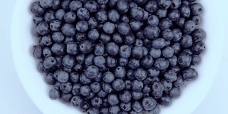 白色的桌子上放着一个盛满成熟、新鲜、多汁的蓝莓的白色盘子。