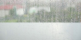 潮湿的窗玻璃，雨点落在模糊的城市背景下的窗玻璃表面