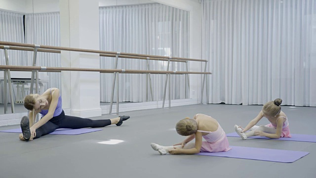在芭蕾舞工作室，女教练向年轻女孩们展示坐姿的斜坡