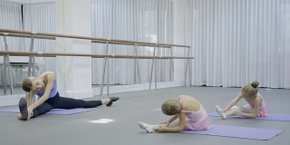 在芭蕾舞工作室，女教练向年轻女孩们展示坐姿的斜坡