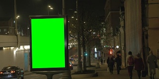 繁忙街道上的一个绿屏广告牌。人们沿着人行道走，