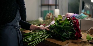 近距离观看的手的女性花商安排现代花束使用美丽的红玫瑰在花店。Slowmotion拍摄