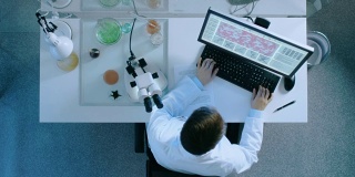 研究科学家在显微镜下观察和在个人电脑中输入新数据的自上而下视图。