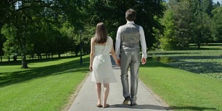 慢镜头:一对年轻的幸福夫妇手牵着手在公园里散步，互相凝视