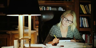 一位戴眼镜的女商人在办公室处理文件。深夜——工作到很晚