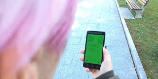 年轻的成年女性在城市街道上使用带绿屏的智能手机