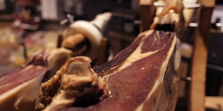 Jamon塞拉诺。传统西班牙火腿在市场上收市。桌上的猪腿火腿。餐厅内部的美食肉。整个火腿放在架子上。摄像机从左向右移动