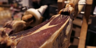 Jamon塞拉诺。传统西班牙火腿在市场上收市。桌上的猪腿火腿。餐厅内部的美食肉。整个火腿放在架子上。摄像机从右向左移动